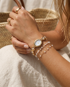 Gold oval-dial pearl-link watch worn on the wrist, summer editorial