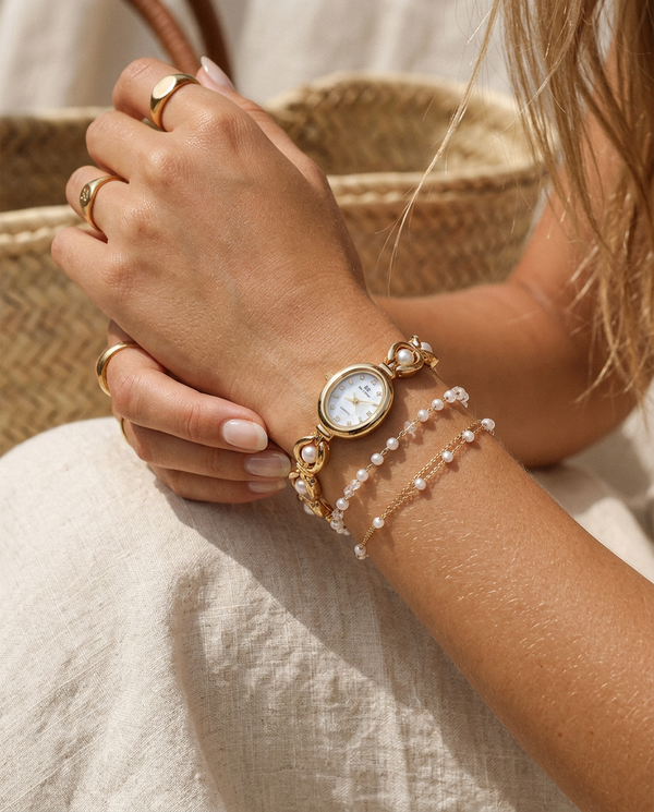 Gold oval-dial pearl-link watch worn on the wrist, summer editorial