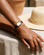 Oval minimal-dial watch with slim black strap worn on the wrist, summer editorial