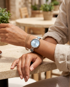 Round minimal-dial stone-link watch with ice-blue face worn on the wrist, summer
