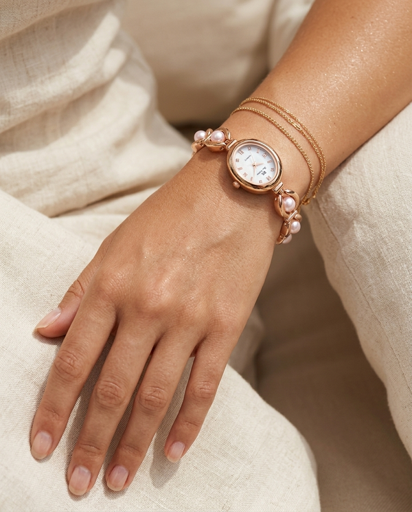 Gold oval-dial watch with soft pink pearl link bracelet worn on the wrist, summer